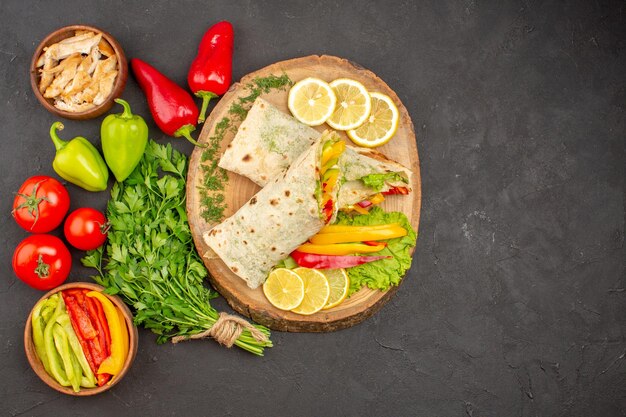 Top view of sliced shaurma meat sandwich with lemonnd greens on black