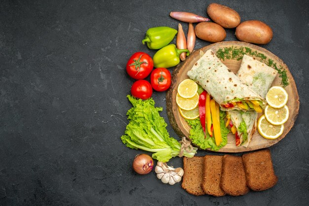 Top view of sliced shaurma sandwich with lemonnd fresh vegetables on black