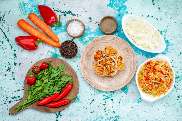 Top view sliced vegetable rolls dough with tasty filling along with greens carrots salad and red spicy peppers on the bright-blue desk food color roll meal snack