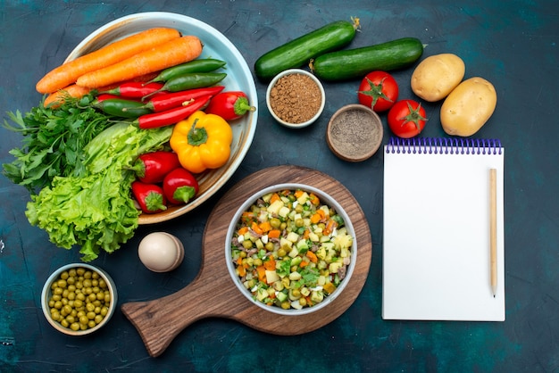 Top view sliced vegetable salad peppered with chicken slices inside plate with fresh vegetables on the dark-blue desk