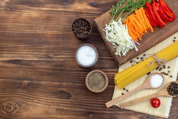 Top view sliced vegetables cabbage carrot greens and pepper on cutting board brown surface