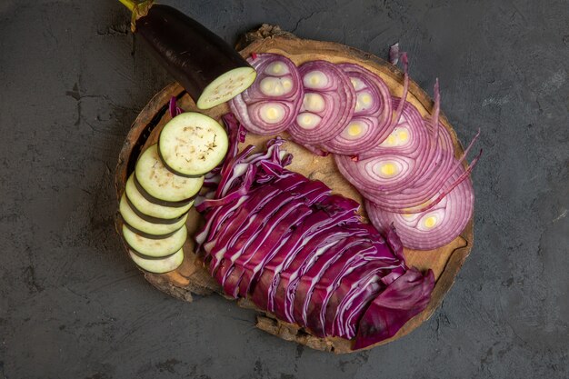 黒に木の板にスライスした野菜赤玉ねぎキャベツとナスのトップビュー