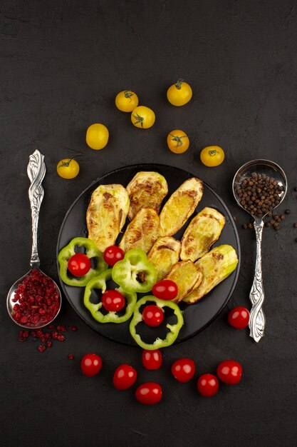 top view sliced vegetables such as green bell pepper and whole red cherry tomatoes inside metallic pan on the dark desk