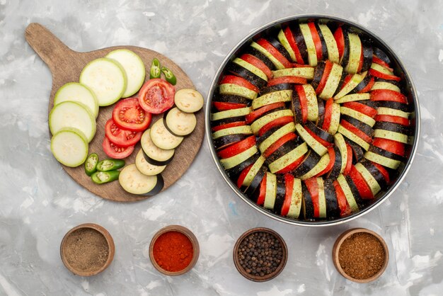 Вид сверху нарезанные овощи, такие как помидоры и баклажаны, свежие и приготовленные на ярком фоне, спелая овощная еда