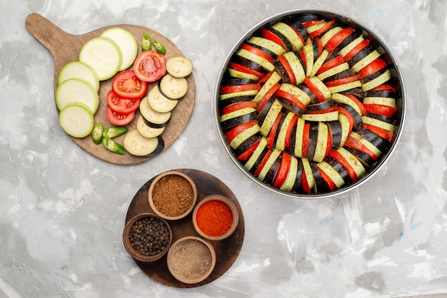 Вид сверху нарезанные овощи, такие как помидоры и баклажаны, свежие и приготовленные на светлом столе, еда из спелых свежих овощей
