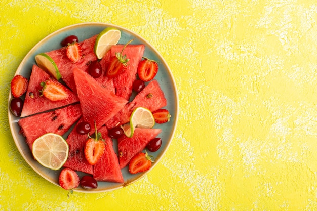 Top view of sliced watermelon with sliced lemons strawberries on the yellow surface