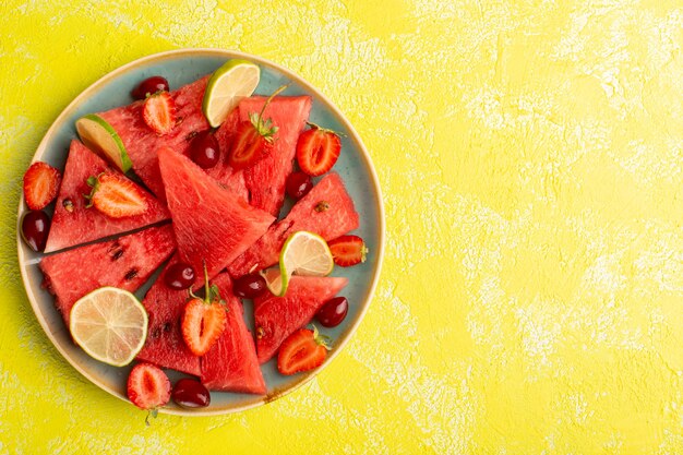 Top view of sliced watermelon with sliced lemons strawberries on the yellow surface