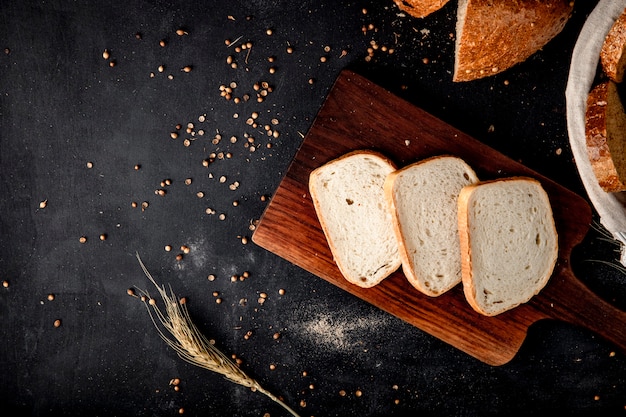 Free photo top view of sliced white bread on cutting board with wheat and sunflower seeds on black surface