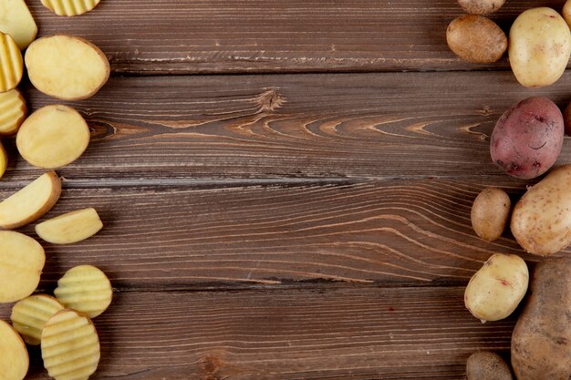 Top view of sliced and whole potatoes on left and right sides and wooden background with copy space