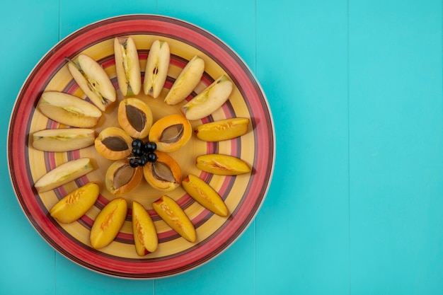 Вид сверху ломтиков абрикоса с яблоками и персиком на тарелке на синей поверхности