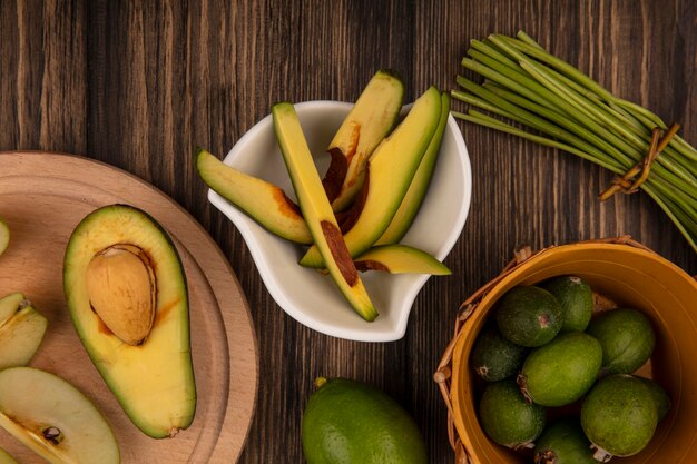 Top view of slices of avocado on a bowl with feijoas on a bucket on a wooden wall