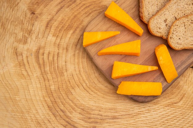 Top view slices of cheese slices of bread on cutting board on wooden table with copy space