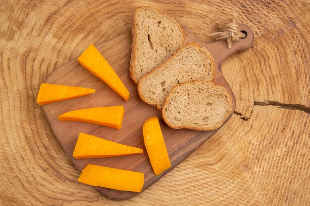 Top view slices of cheese slices of bread on cutting board on wooden table