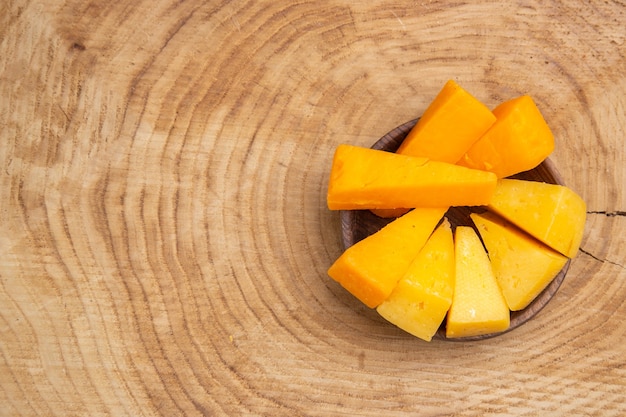 Top view slices of cheese in wooden bowl on wooden table with copy space