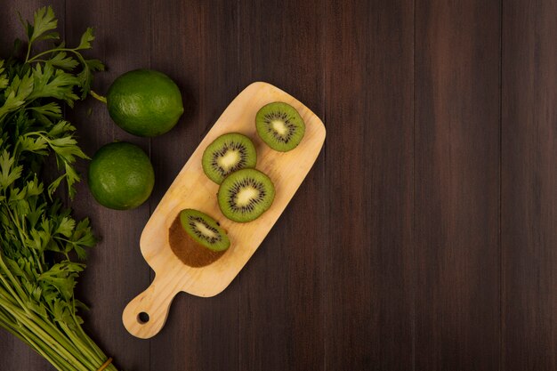 Top view of slices of kiwi on a wooden kitchen board with parsley and limes isolated on a wooden background with copy space