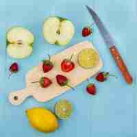 Foto gratuita vista dall'alto di fette di fragola su una tavola di cucina in legno con coltello con mela a fette su sfondo blu