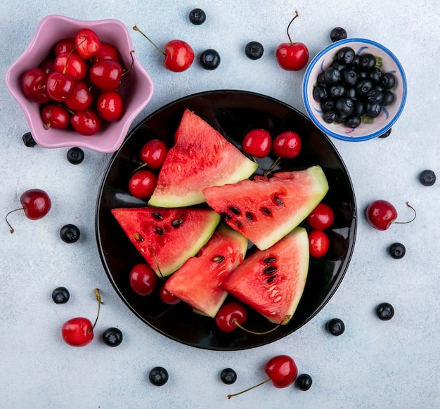 Top view slices of watermelon on a plate with blueberries and cherries