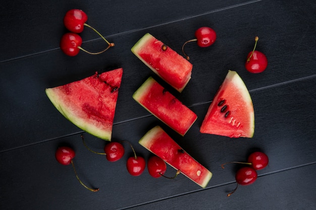 Top view slices of watermelon with cherries on a black background