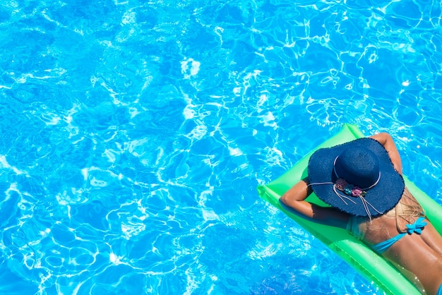 Вид сверху стройной молодой женщины в бикини на зеленом надувном матрасе в бассейне
