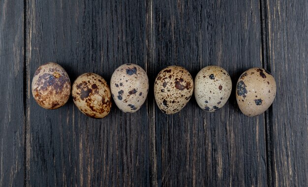 Top view of small fresh quail eggs arranged in a line on a wooden background