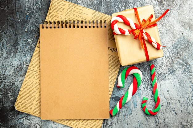 회색 표면에 신문 크리스마스 사탕에 빨간 리본 노트북으로 묶인 상위 뷰 작은 선물