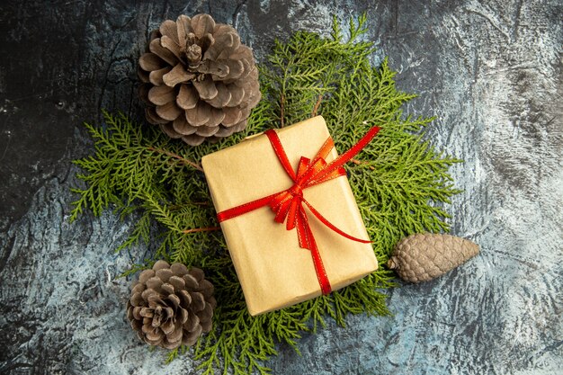 Top view small gift tied with red ribbon on pine branches pinecones on dark surface