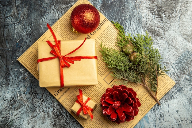 Top view small gift tied with red ribbon red ball pine branch on newspaper on dark surface