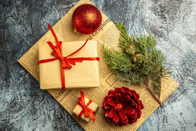 Top view small gift tied with red ribbon red ball pine branch on newspaper on dark surface