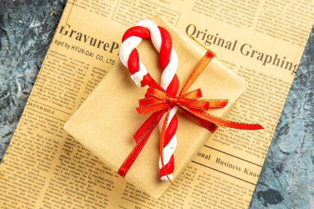 top view small gift tied with red ribbon and xmas candy on newspaper on grey surface