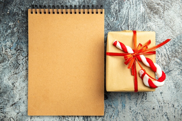 Вид сверху небольшой подарок, перевязанный красной лентой, блокнот с рождественскими конфетами на серой поверхности