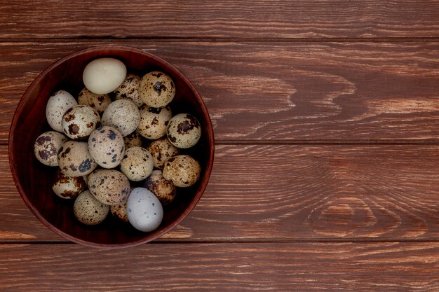 Top view of small quail eggs on a wooden bowl on a wooden background with copy space