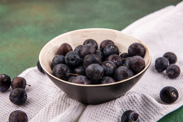 Free photo top view of the small sour blue-black fruit sloes on a bowl on white tablecloth on a green background