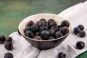 Foto gratuita vista dall'alto delle piccole prugnole di frutta blu-nere acide su una ciotola sulla tovaglia bianca su sfondo verde