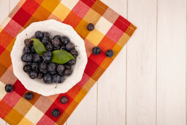 Top view of the small sour blue-black fruit sloes on a white bowl on a colorful checked tablecloth on a white background