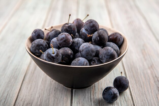 Top view of the small sour blue-black sloes on a black bowl on a grey wooden background