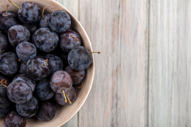 Top view of the small sour blue-black sloes on a bowl on a wooden background with copy space