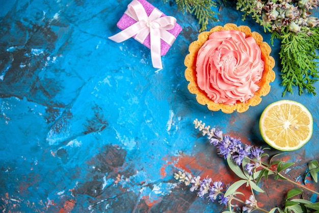 Top view of small tart with pink pastry cream lemon slice on blue surface