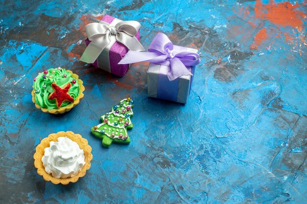 Top view small tarts small gifts xmas tree biscuit on blue red table copy place