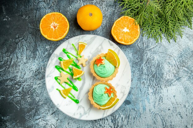 Top view small tarts with green pastry cream and lemon slice on plate cut oranges notepad on dark table