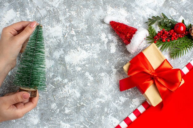 Top view small xmas tree in female hand small santa hat present on grey white table