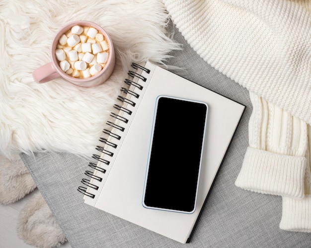 Top view of smartphone and notebook with cup of hot cocoa