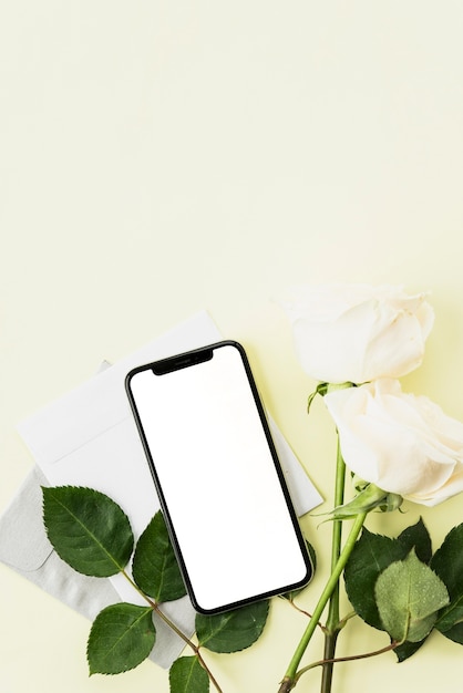 Top view of smartphone; white roses and envelope on yellow backdrop