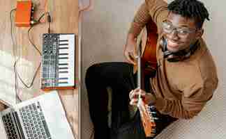 Free photo top view of smiley male musician at home playing guitar and mixing with laptop