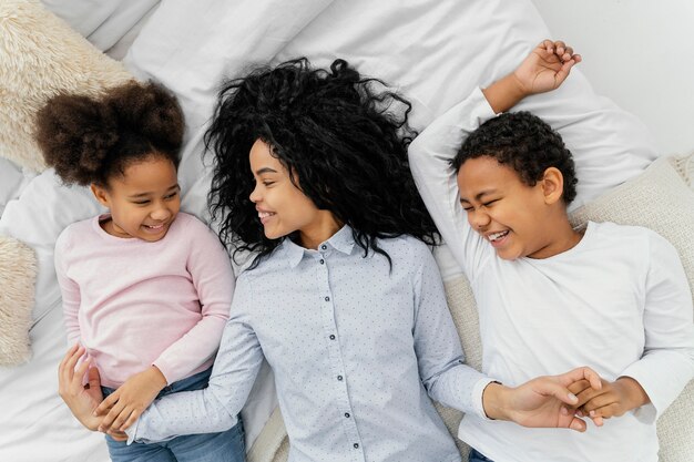 Top view of smiley mother staying in bed at home with her children