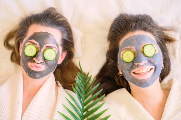 Top view of smiley women with face masks and cucumber slices on their eyes