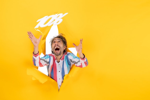 Top view of smiling bearded man playing with ten percentage numbers in a torn hole in yellow paper
