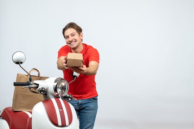 Top view of smiling delivery guy in red uniform standing near scooter giving order on white background