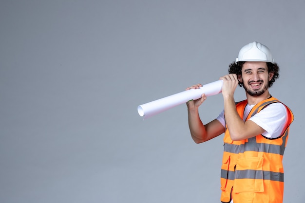 Top view of smiling happy male constructor in warning vest wearing safety helmet and holding blank on gray wave wall