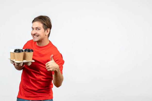 Top view of smiling happy young man in red blouse holding orders and making ok gesture on white wall