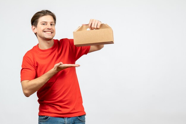 Top view of smiling and happy young man in red blouse showing box on white wall